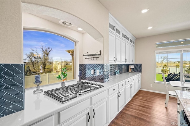 kitchen featuring stainless steel gas cooktop, white cabinetry, light countertops, decorative backsplash, and dark wood-style floors