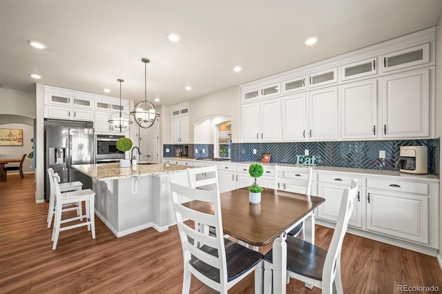 kitchen with appliances with stainless steel finishes, arched walkways, white cabinets, and a center island with sink