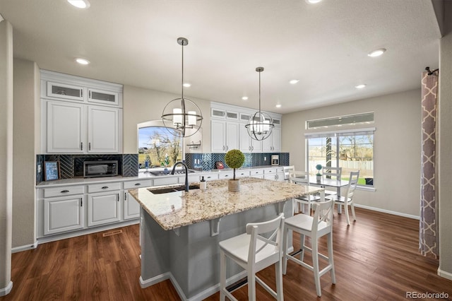 kitchen with backsplash, an island with sink, dark wood-style floors, white cabinetry, and a sink