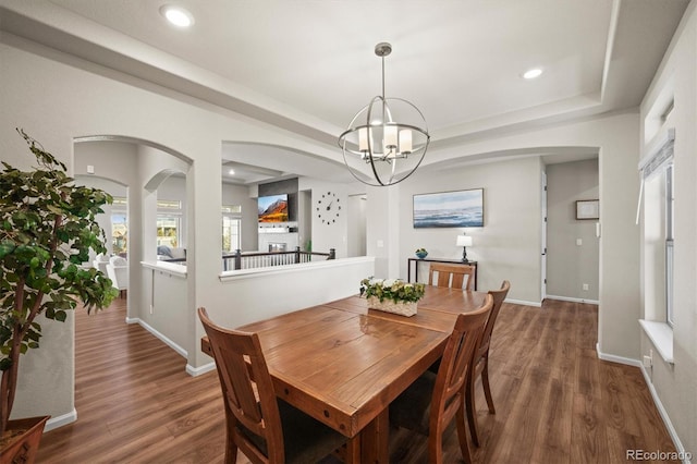 dining room with arched walkways, a notable chandelier, a raised ceiling, and wood finished floors