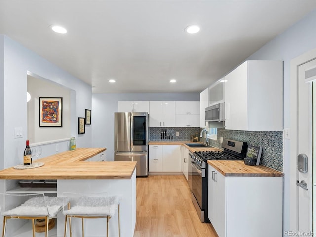 10109 W 68th Ave, Arvada, CO 80004 - kitchen featuring wooden counters, appliances with stainless steel finishes, white cabinets, a sink, and backsplash
