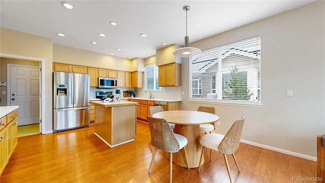 kitchen featuring light wood finished floors, stainless steel appliances, light countertops, a sink, and a kitchen island