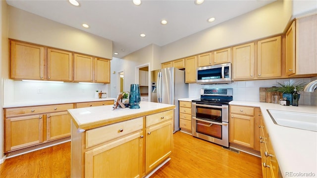 kitchen featuring light countertops, backsplash, a sink, light wood-style flooring, and appliances with stainless steel finishes