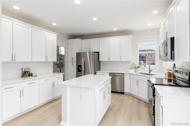 kitchen featuring a center island, appliances with stainless steel finishes, white cabinets, a sink, and light wood-type flooring