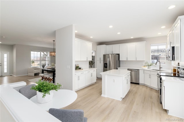 kitchen featuring light wood finished floors, appliances with stainless steel finishes, open floor plan, a sink, and a kitchen island