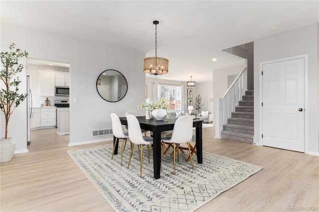 dining area featuring light wood-type flooring, stairway, baseboards, and visible vents