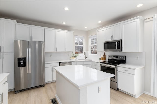 kitchen featuring light wood finished floors, stainless steel appliances, visible vents, white cabinetry, and a sink