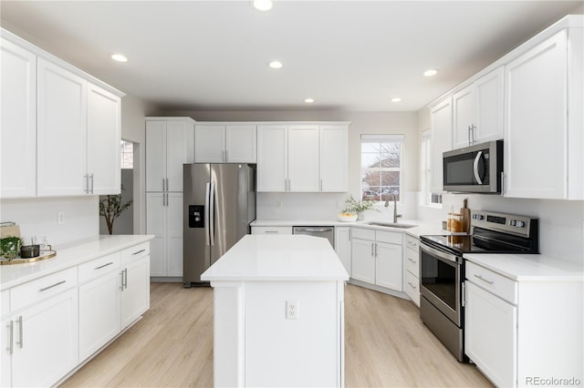 kitchen with stainless steel appliances, a center island, light wood-style floors, and a sink