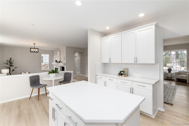 kitchen with white cabinets, open floor plan, a center island, light countertops, and light wood-type flooring