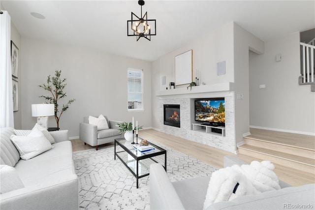 living area featuring baseboards, a tile fireplace, stairway, light wood-style floors, and a notable chandelier