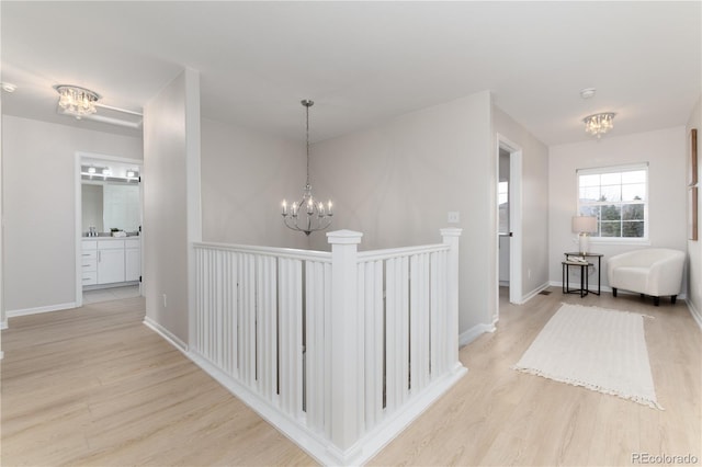 hallway featuring baseboards, light wood-style flooring, and a notable chandelier