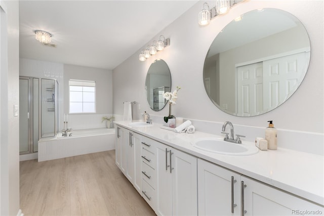 bathroom with a garden tub, wood finished floors, a stall shower, and a sink