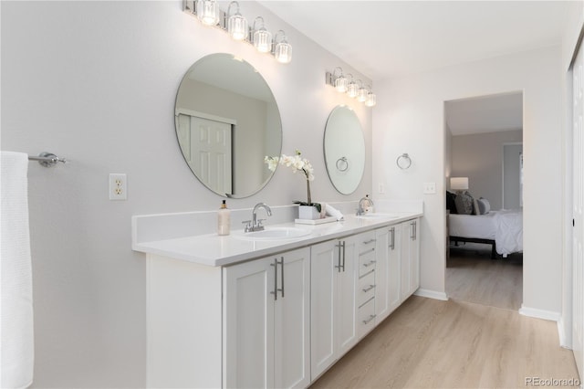 bathroom featuring double vanity, ensuite bath, a sink, and wood finished floors