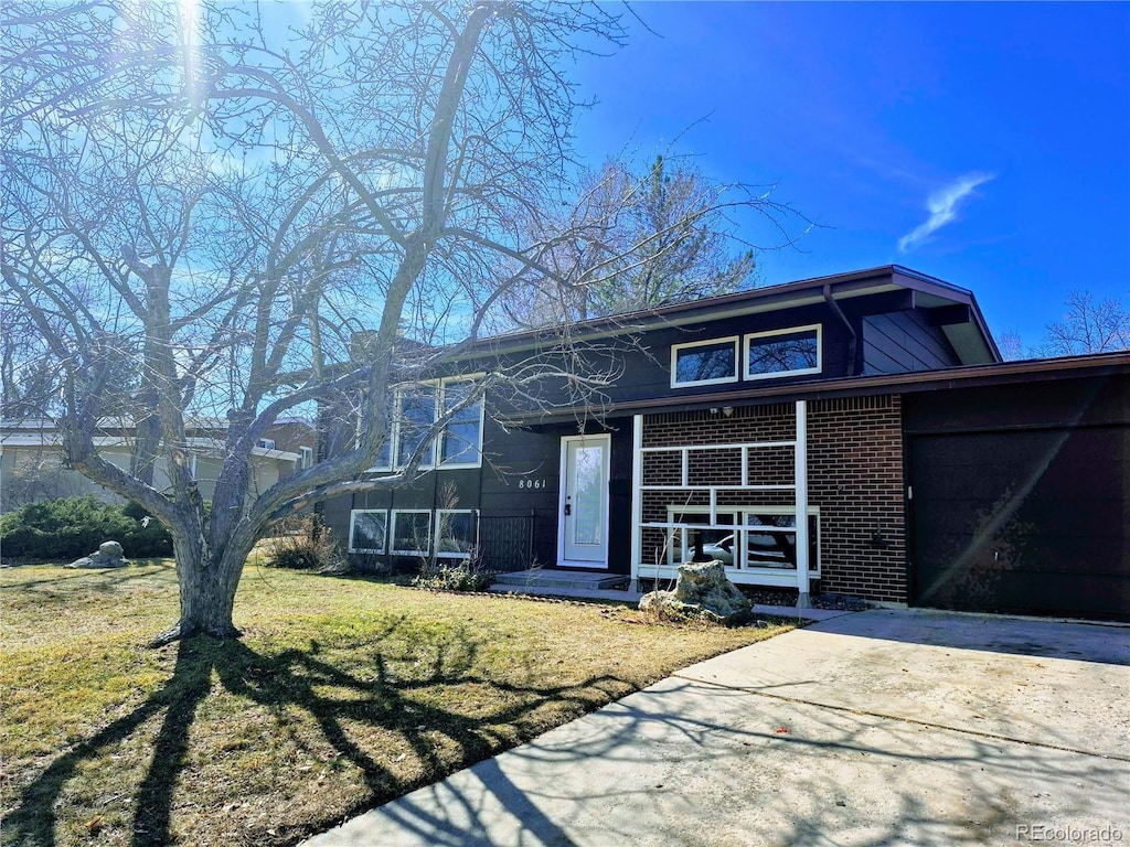 view of front of home featuring a porch, a front yard, brick siding, and driveway