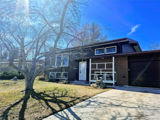 view of front of home featuring a porch, a front yard, brick siding, and driveway