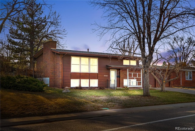 view of front of property featuring brick siding, a lawn, a chimney, a garage, and driveway