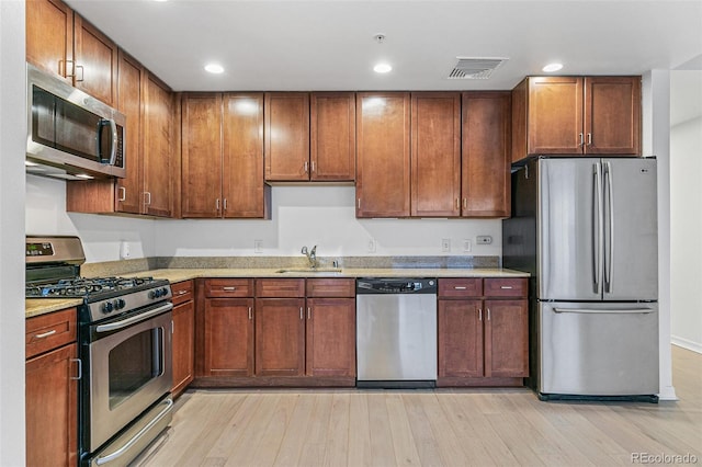 kitchen with light stone counters, appliances with stainless steel finishes, sink, and light wood-type flooring