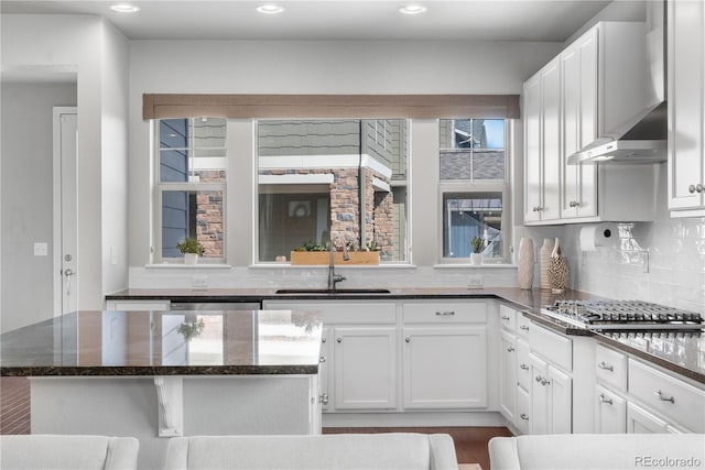 kitchen featuring wall chimney range hood, tasteful backsplash, stainless steel gas stovetop, white cabinetry, and sink