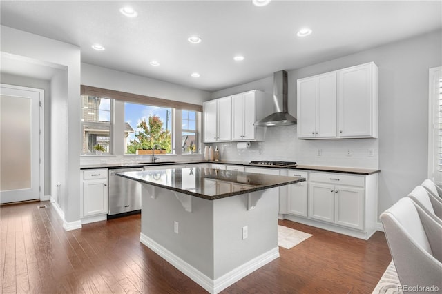 kitchen featuring wall chimney range hood, appliances with stainless steel finishes, a center island, white cabinets, and dark hardwood / wood-style floors