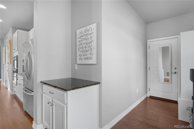 kitchen with dark wood-type flooring, dark stone counters, stainless steel fridge, and white cabinets