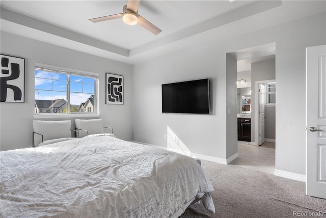 bedroom with ceiling fan, light colored carpet, a tray ceiling, and ensuite bath