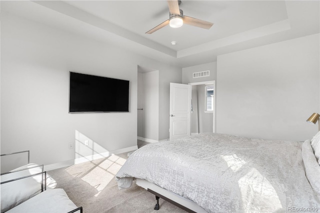 carpeted bedroom with a raised ceiling and ceiling fan