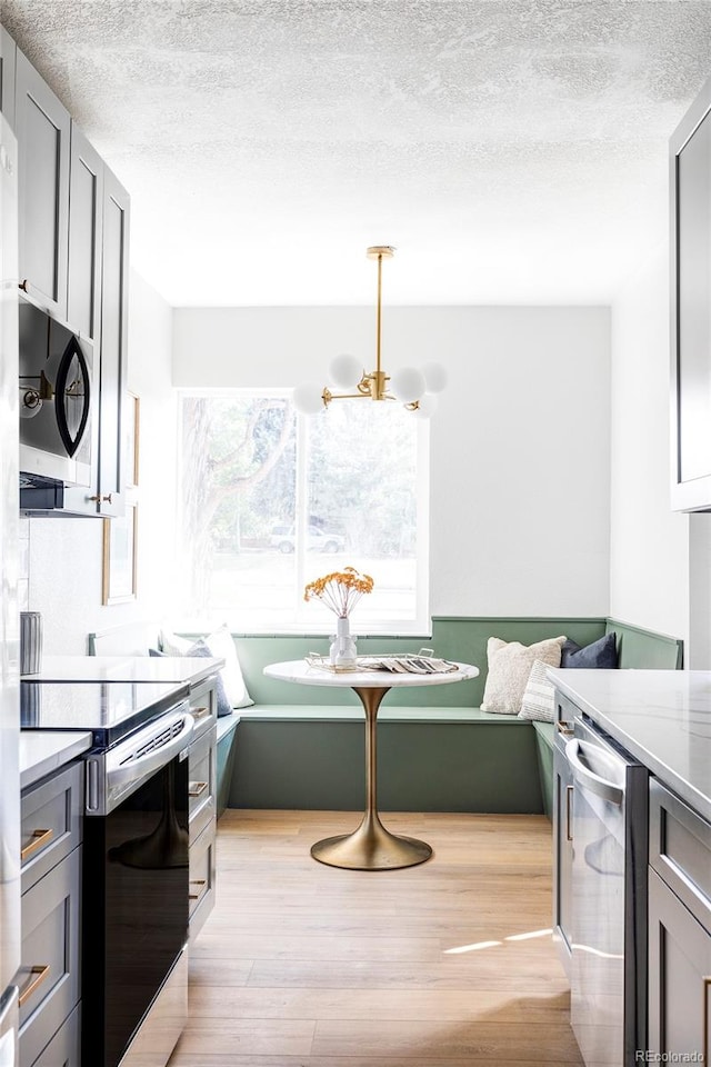 kitchen featuring gray cabinetry, light hardwood / wood-style flooring, appliances with stainless steel finishes, breakfast area, and a textured ceiling