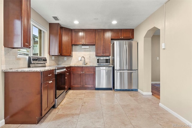 3925 Pecos St, Denver, CO 80211 - kitchen with appliances with stainless steel finishes, arched walkways, backsplash, baseboards, and light stone countertops