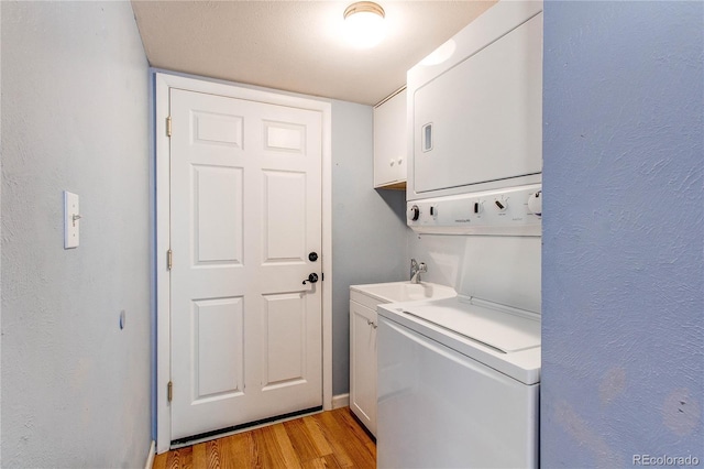 laundry room with cabinet space, a textured wall, light wood-style flooring, a sink, and stacked washing maching and dryer