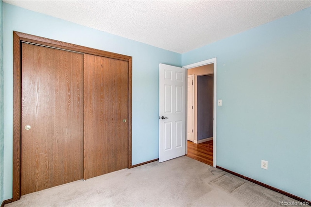 unfurnished bedroom featuring a textured ceiling, baseboards, a closet, and light colored carpet