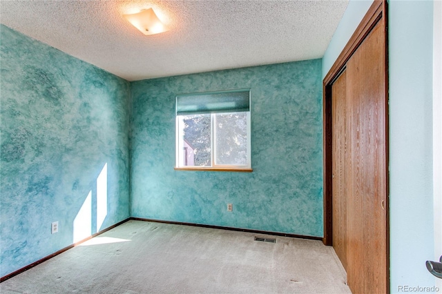 unfurnished room with baseboards, carpet flooring, visible vents, and a textured ceiling