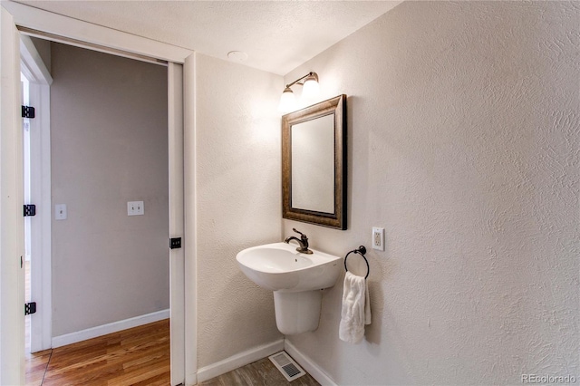 bathroom with visible vents, baseboards, wood finished floors, and a textured wall