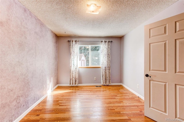 unfurnished room with baseboards, a textured ceiling, visible vents, and light wood-style floors