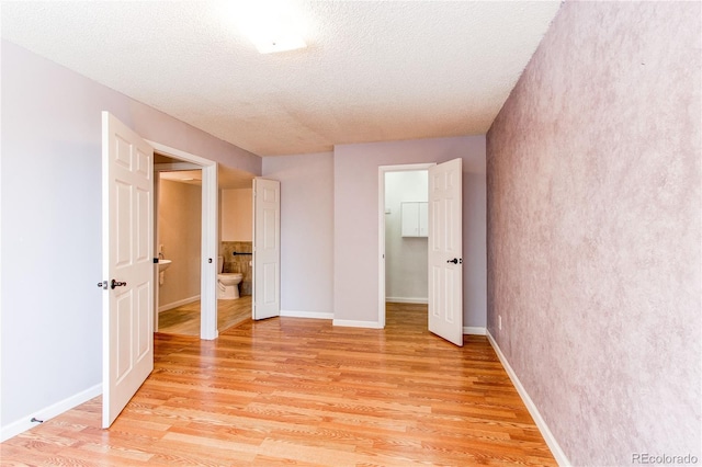 unfurnished bedroom featuring a textured ceiling, light wood-type flooring, a walk in closet, and baseboards