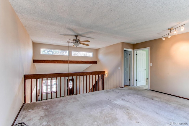 empty room featuring a textured ceiling, ceiling fan, carpet flooring, baseboards, and rail lighting