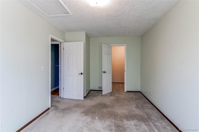 unfurnished bedroom featuring a textured ceiling, carpet flooring, attic access, and baseboards