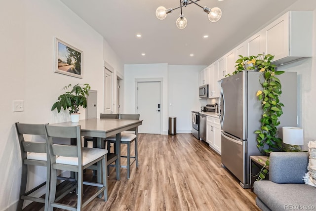 kitchen featuring light wood-type flooring, white cabinets, stainless steel appliances, and an inviting chandelier