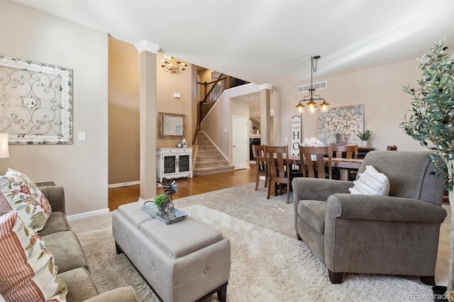 living room featuring visible vents, a notable chandelier, ornate columns, and stairs