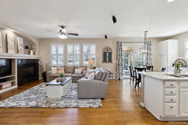 living room with a textured ceiling, wood finished floors, ceiling fan with notable chandelier, and a glass covered fireplace