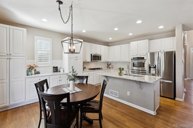 kitchen with stainless steel appliances, an island with sink, visible vents, and white cabinetry