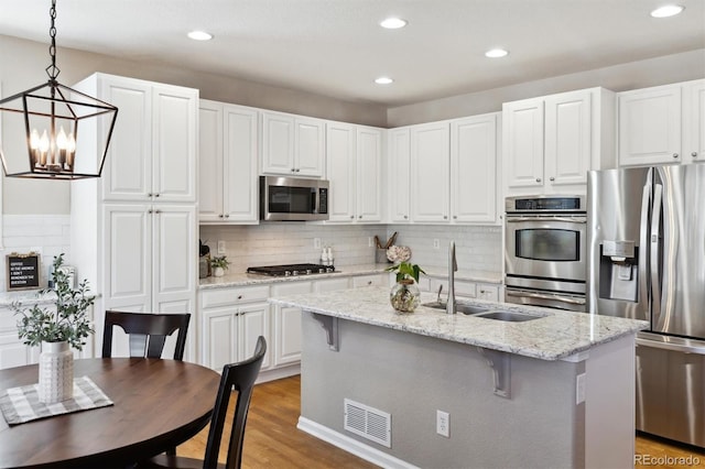 kitchen featuring light wood-style flooring, stainless steel appliances, a sink, visible vents, and backsplash