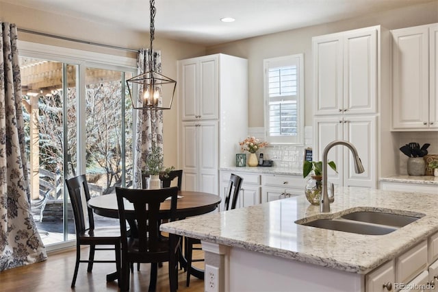 kitchen featuring wood finished floors, hanging light fixtures, a sink, white cabinetry, and backsplash