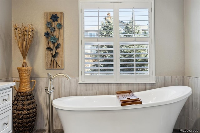 bathroom with a textured wall, a wainscoted wall, a freestanding bath, and vanity