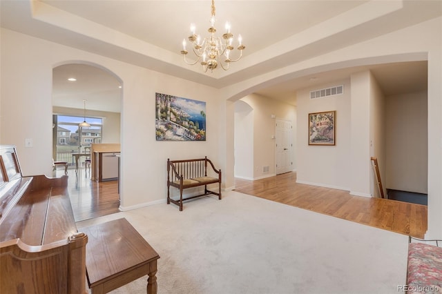 living area with arched walkways, a tray ceiling, baseboards, and visible vents