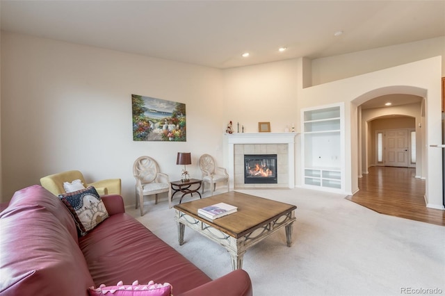 living room with built in shelves, a fireplace, recessed lighting, arched walkways, and carpet