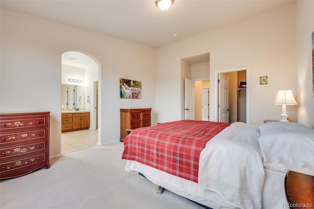 bedroom featuring connected bathroom, a closet, light carpet, a walk in closet, and arched walkways