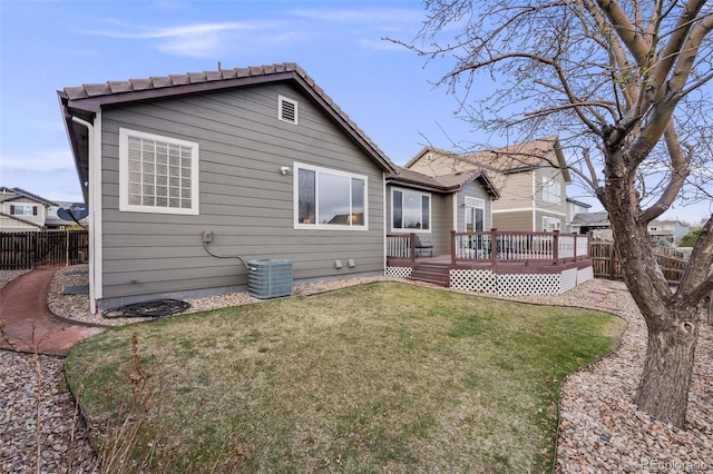 rear view of house featuring a tile roof, a fenced backyard, a deck, central AC, and a lawn