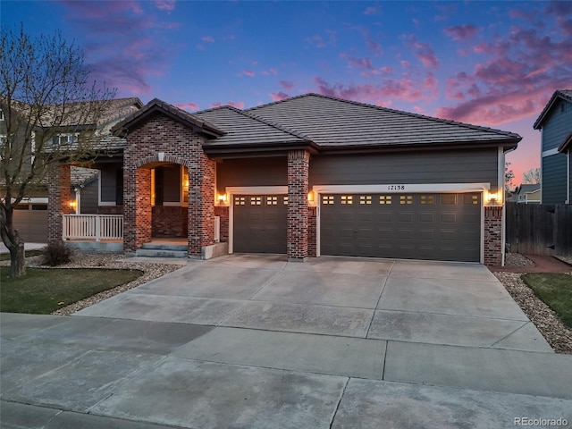 view of front of home with a tile roof, driveway, covered porch, an attached garage, and brick siding