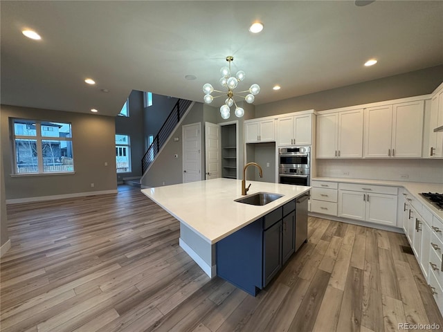 kitchen featuring sink, stainless steel appliances, white cabinetry, light hardwood / wood-style flooring, and an island with sink