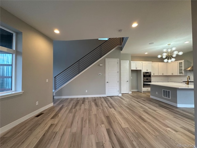 unfurnished living room featuring sink, light wood-type flooring, and a notable chandelier